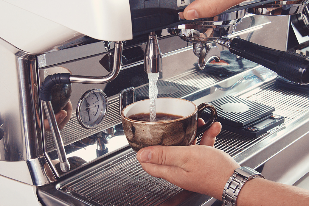 Hands operating a professional espresso machine, pulling a shot into a ceramic cup