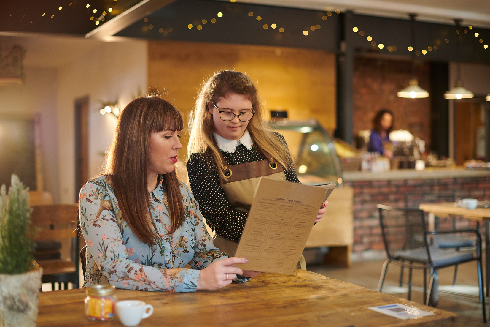 A café server presenting a menu to a smiling customer at a wooden table