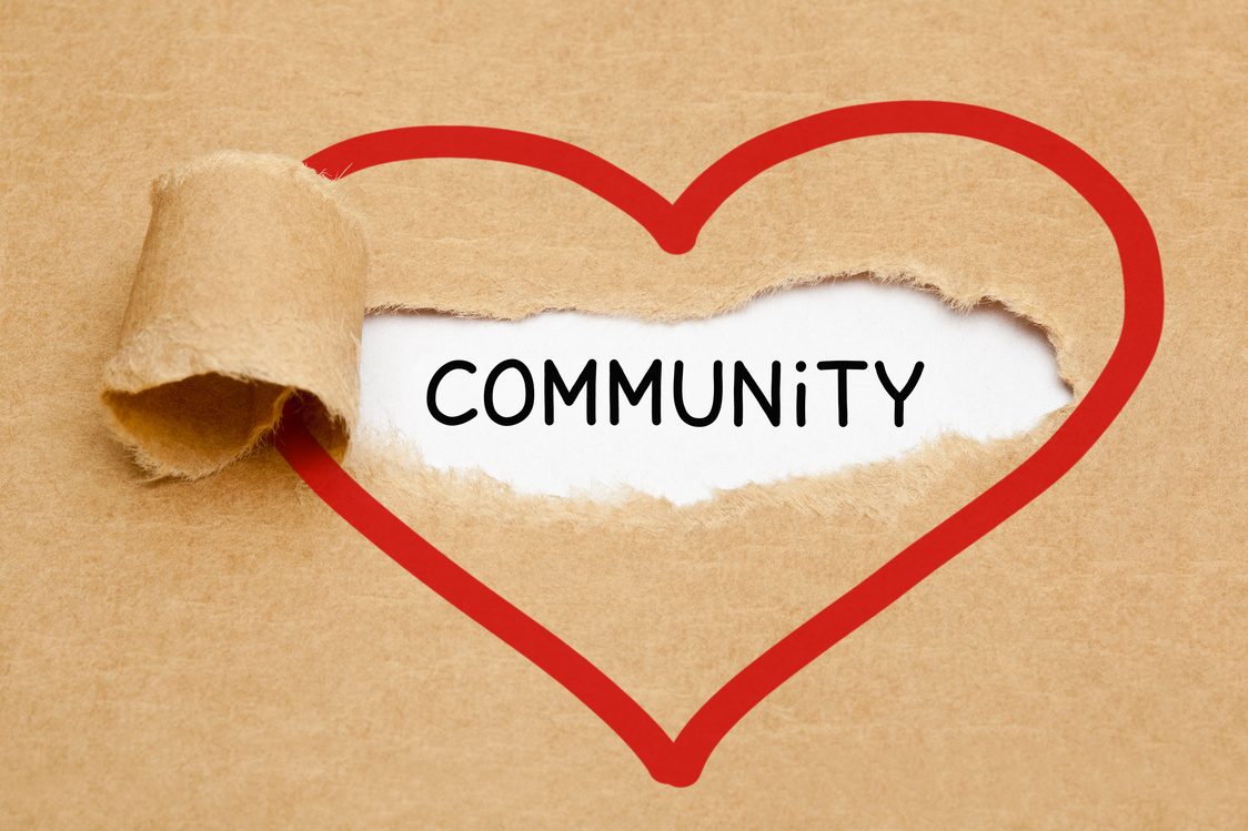 The word COMMUNITY revealed beneath torn craft paper with a red heart outline
