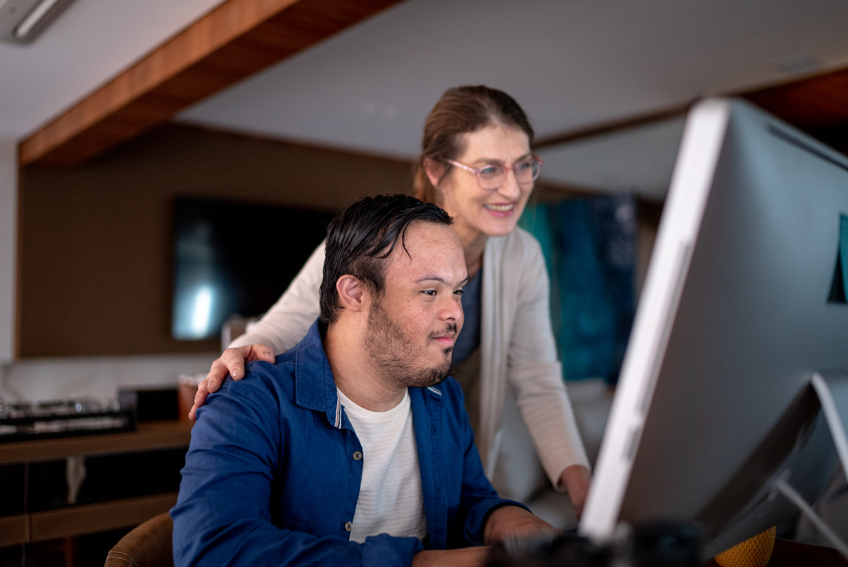 Two people looking at a computer screen together, the older woman smiling supportively